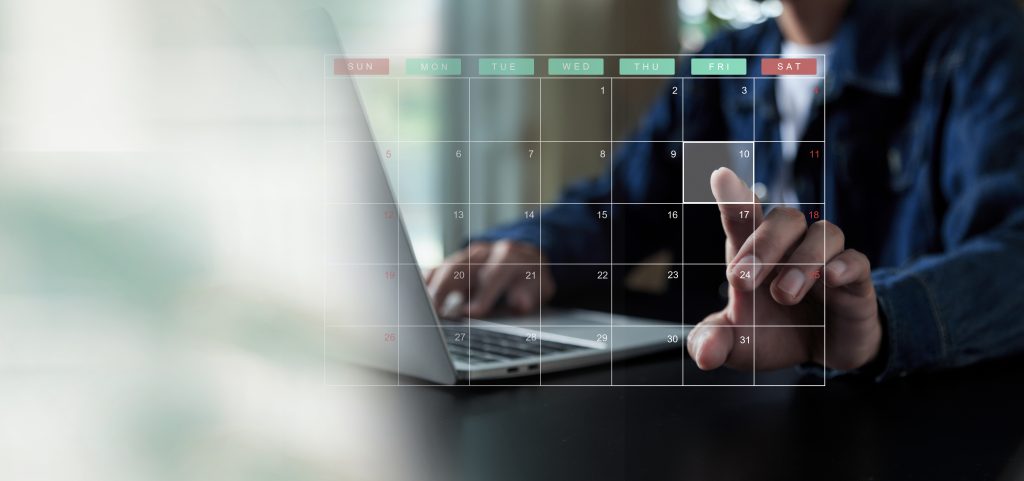 Main d’une personne pointant une date sur un calendrier numérique affiché sur un ordinateur portable, symbolisant la planification et la régularité dans la démarche qualité.